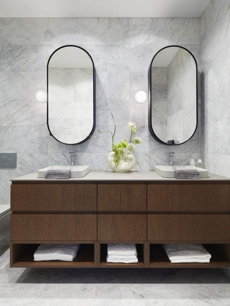 Features floating wood veneer vanities, oval medicine cabinets, and wall-mounted makeup lights.